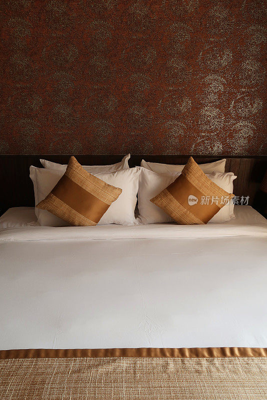 豪华的特大号床，金色的散垫和白色的枕头/折叠床单，木质床头板靠在带有金色图案设计的特色墙上